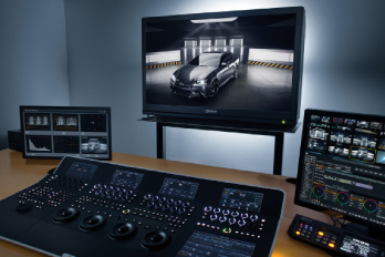 Video editing workstation with a large monitor showing a car, a control surface, and two smaller screens.