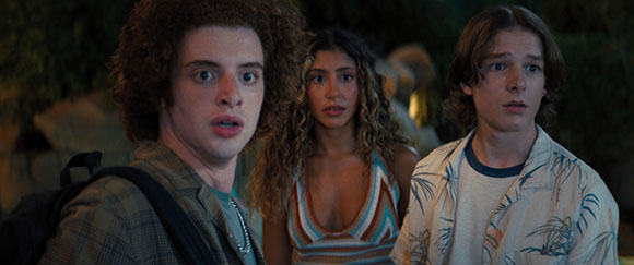Three teenagers with shocked expressions looking toward the side in a dark outdoor setting.