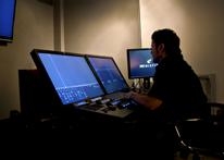 A person sits in a dark room operating a workstation with three computer monitors.
