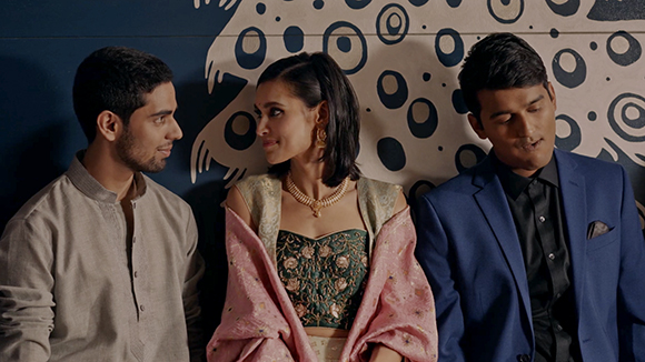 A man in a tan shirt, a woman in traditional Indian attire, and a man in a blue suit pose together.