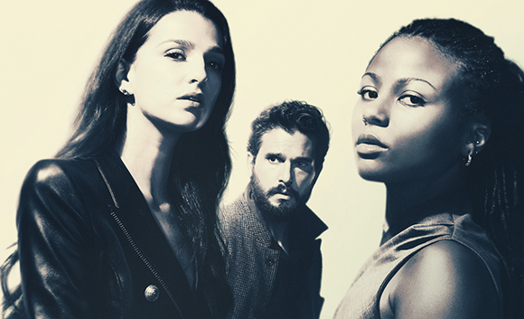 A black and white portrait of a woman in leather, a man in a textured jacket, and a woman in a sleeveless top.