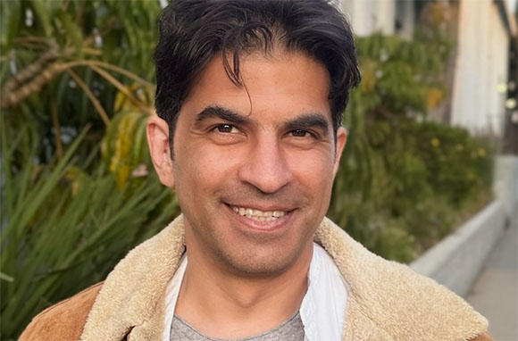 A man with dark hair smiling at the camera outdoors.