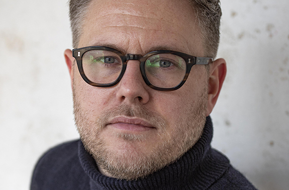 A man with short light hair and glasses looking directly at the camera.