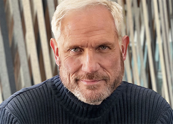Close-up portrait of a middle-aged man with short blonde hair and a salt-and-pepper beard looking at the camera.