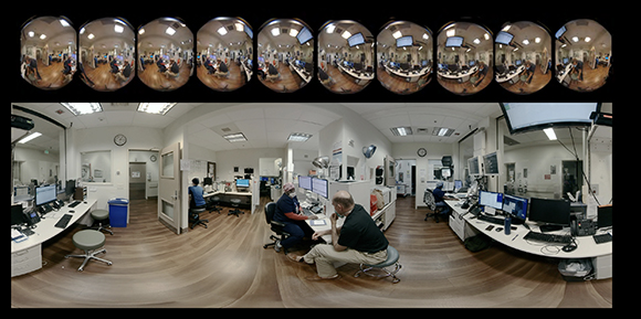 A wide panoramic view of a command center with multiple workstations, computer monitors, and staff members.