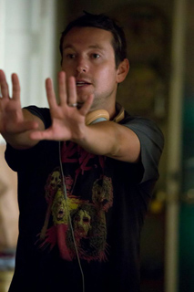 A man in a black graphic t-shirt holds both hands up with palms facing forward.