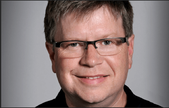 A smiling man with short brown hair and black-rimmed glasses looking directly at the camera.