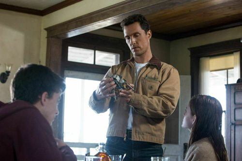 A man in a tan jacket holds a small object while sitting at a table with two other people.