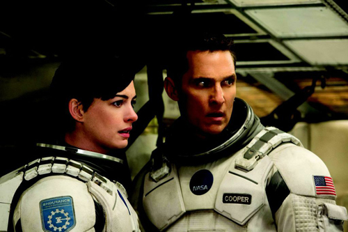 Two astronauts in white NASA spacesuits looking forward with serious expressions inside a spacecraft.