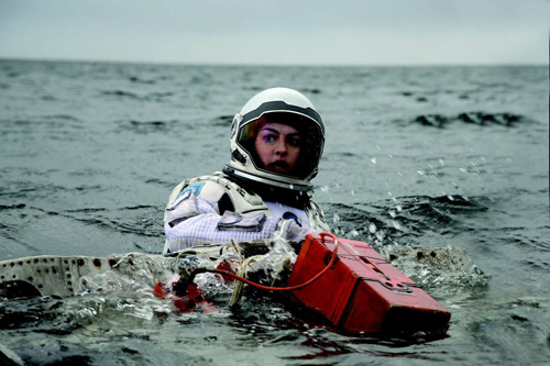 A person in a white astronaut suit floats in dark, choppy ocean water.
