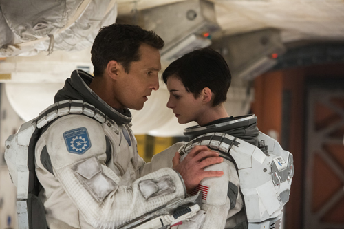 A man and a woman in white spacesuits look intensely at each other in a spacecraft.