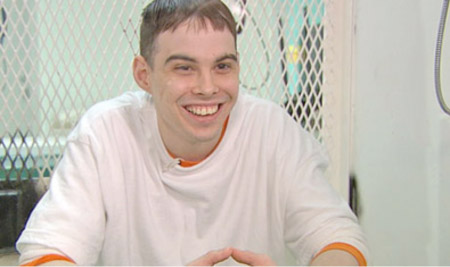 A man with short brown hair smiling while wearing a white long-sleeved shirt.