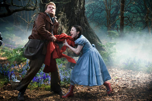 A man in a brown jacket and a girl in a blue dress tugging on a red cloth in a foggy forest.
