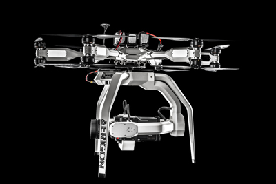 A white multi-rotor drone with four large propellers and a stabilized camera system suspended underneath.