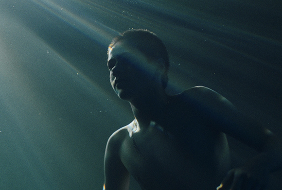 Silhouette of a man underwater with bright light rays streaming down from the surface.