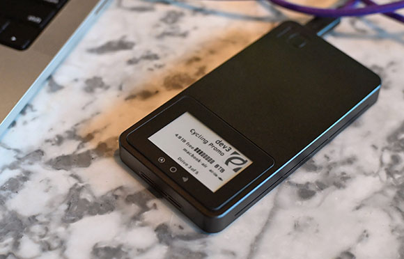 A black external hard drive with a small digital display sits on a white marble countertop next to a laptop.