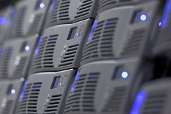 Close-up of multiple dark grey server units stacked in rows with small blue indicator lights.
