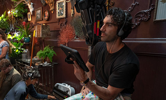 A man wearing headphones looks away from a tablet he is holding in a room with ornate decor.