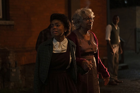 A young woman and an older woman with white hair stand together outdoors at night.