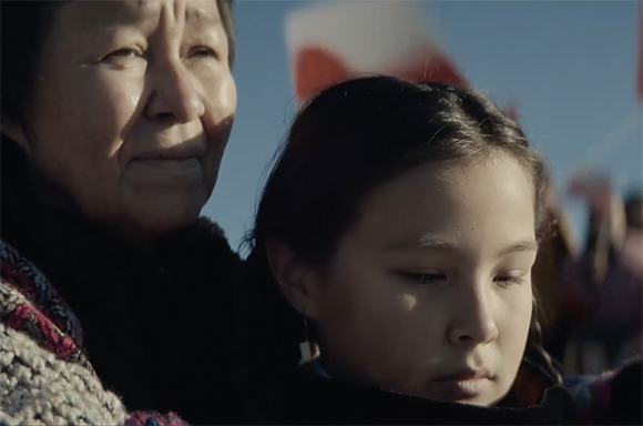 Close-up of an older woman and a young girl with serious expressions outdoors under a blue sky.