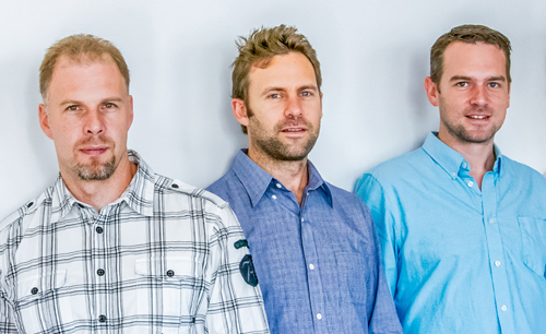 Three men standing in a row wearing plaid and button-down shirts.