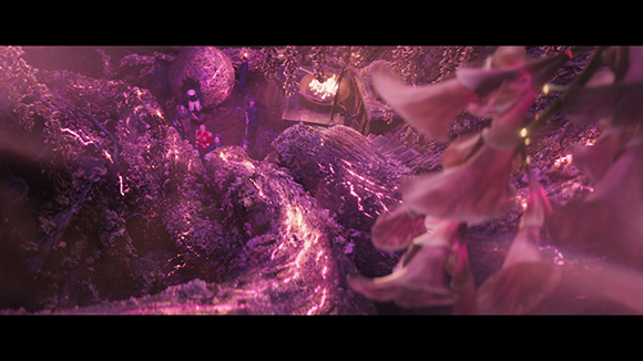 A wide shot of a purple, rocky landscape with small figures and glowing pink flowers in the foreground.