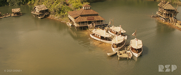 Aerial view of rustic wooden buildings and several white paddle boats docked along a riverbank.