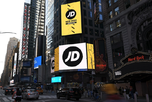 Large yellow and white JD Sports advertisements on skyscrapers in a busy city street.