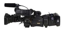 A professional black JVC video camera with a large lens and a shotgun microphone attached on top.