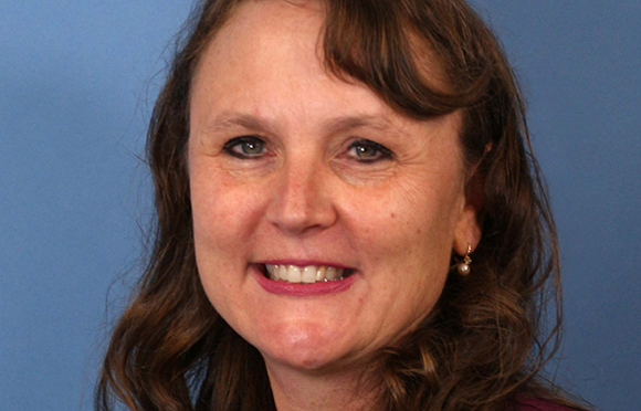 A smiling woman with wavy brown hair and blue eyes against a solid blue background.