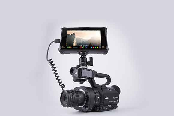 A black JVC professional video camera with an attached external monitor displaying a mountain landscape.