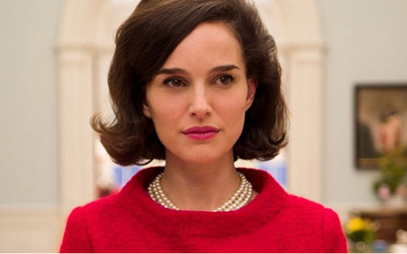 A woman with dark hair wearing a red top and pearl necklace looks ahead with a neutral expression.