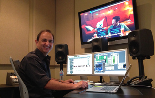 A man sits at a desk with multiple computer monitors and studio speakers in a production studio.