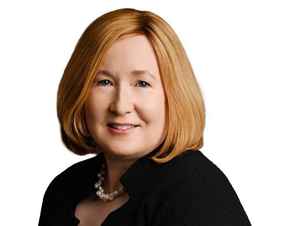 A woman with shoulder-length strawberry blonde hair, wearing a black blazer and a pearl necklace.