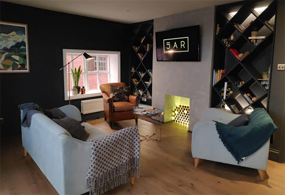 A living room with dark walls, two light blue armchairs, a brown leather chair, and diamond-patterned shelving.