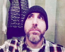 A man with a beard and black beanie looking up, wearing a plaid shirt.