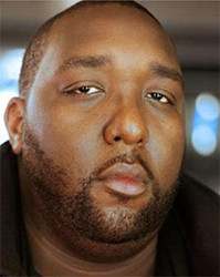 Close-up portrait of a Black man with a short beard looking forward.