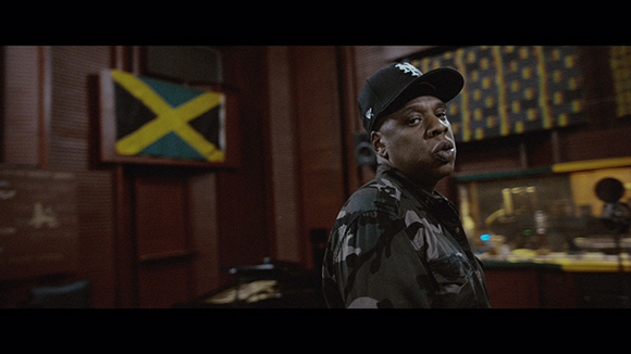 A man wearing a black baseball cap and camouflage shirt looks toward the camera in a studio.