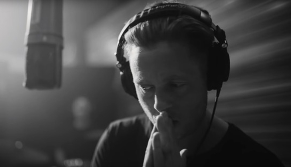 Black and white close-up of a man wearing large headphones in a studio near a microphone.