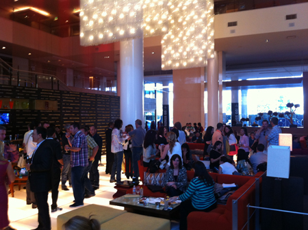 A group of people mingling in a large, modern lobby area with contemporary seating and large, decorative chandeliers hanging