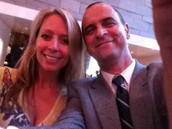 A smiling woman with blonde hair and a smiling man in a suit and tie pose for a selfie.