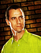 A man with short dark hair wearing a lime green button-down shirt, looking slightly to the side.