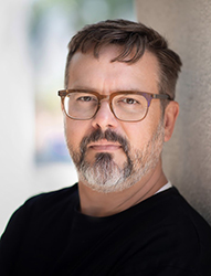 A man with brown hair, glasses, and a salt-and-pepper beard looking at the camera.