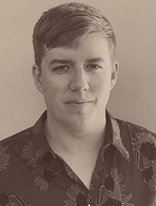 A man with short hair wearing a dark floral patterned button-down shirt.