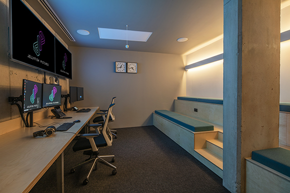 A workspace with long wooden desks, multiple computer monitors, and built-in wooden benches with blue cushions.