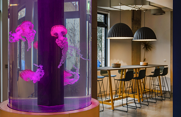 A tall, glowing purple cylinder filled with pink jellyfish, positioned next to a modern dining area.