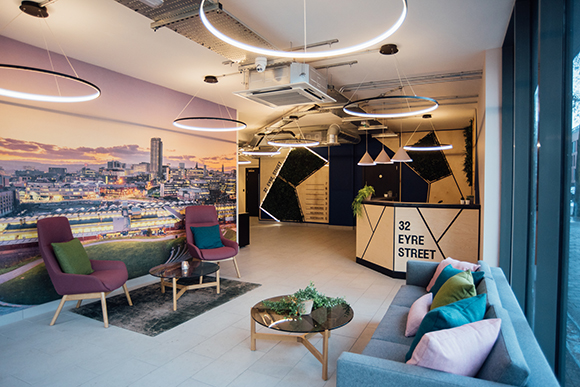 Modern lounge with a cityscape mural, colorful armchairs, a grey sofa, and circular ring lights.