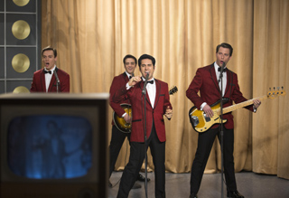 Four men in matching red blazers and black trousers perform music on a stage with gold curtains.
