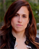 A woman with long wavy brown hair and hoop earrings looking directly at the camera.