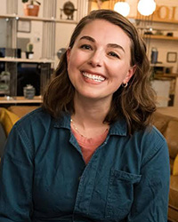 A smiling woman with shoulder-length brown hair wearing a blue button-down shirt.
